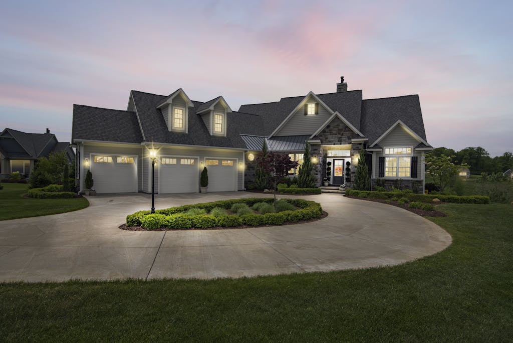 A modern suburban home at dusk, beautifully lit with exterior lights and three garage doors.